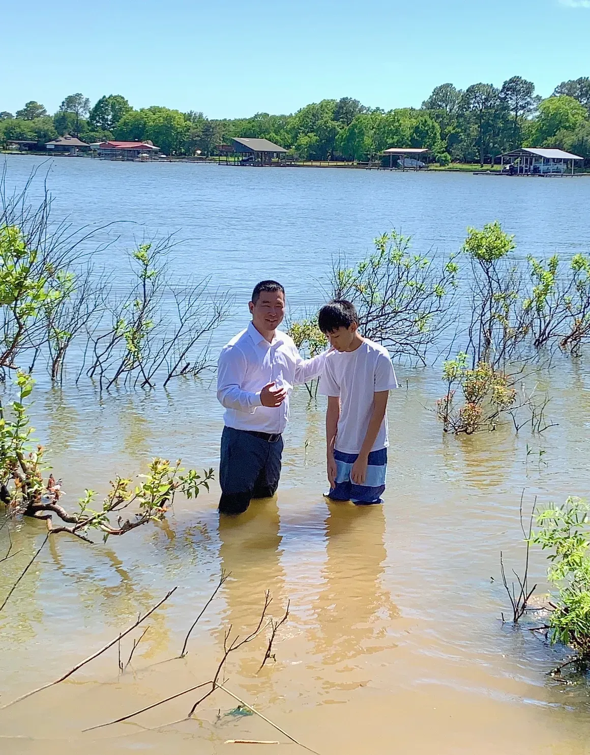 A minister and baptism candidate standing together in a lake